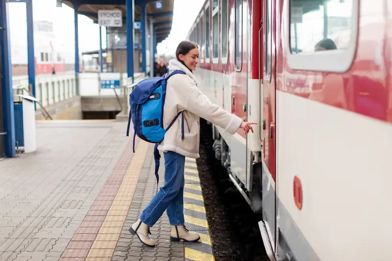 Frau mit Rucksack steigt am Bahnsteig in einen roten Zug ein