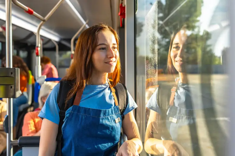Junge Frau mit Rucksack steht im Stadtbus und schaut aus dem Fenster