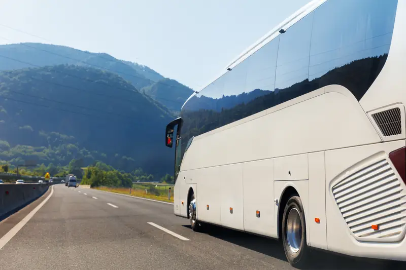 Weißer Reisebus fährt auf einer Autobahn vor Bergen